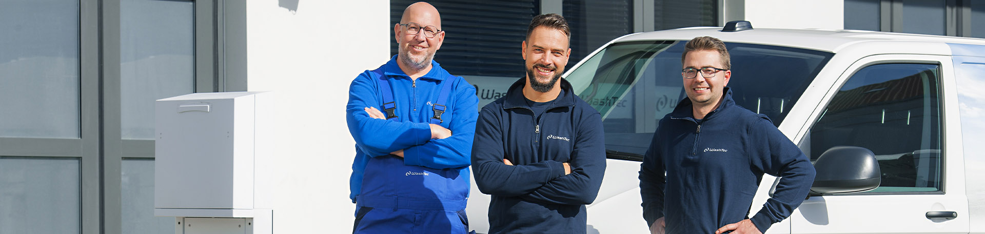 Drei Personen stehen vor einem WashTec Wagen und lächeln mit verschränkten Armen in die Kamera.