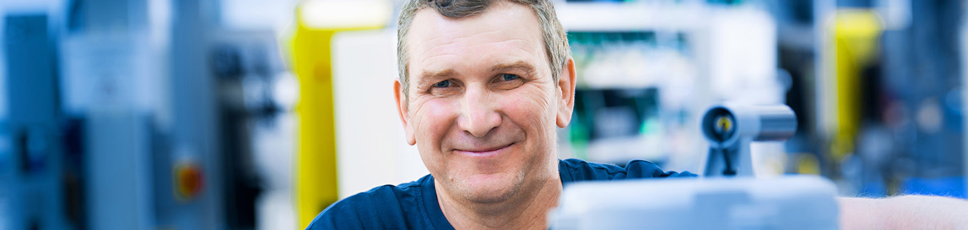 Eine Person steht in einer Produktionshalle und lächelt in die Kamera.