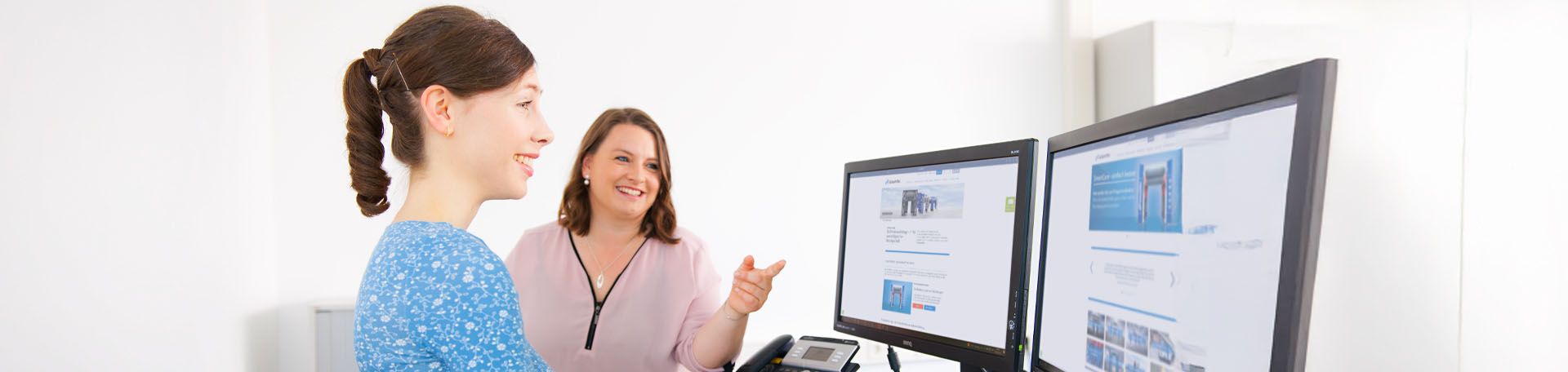 Zwei Personen sitzen seitlich zur Kamera, blicken auf einen Bildschirm und lächeln.