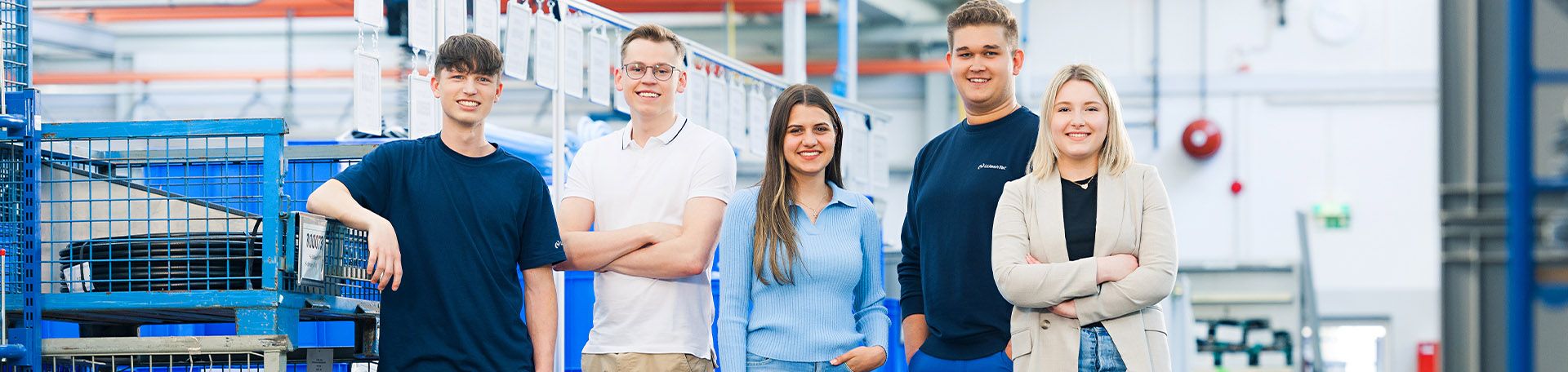 Eine Gruppe junger Personen steht in einer Produktionshalle und lächelt in die Kamera.