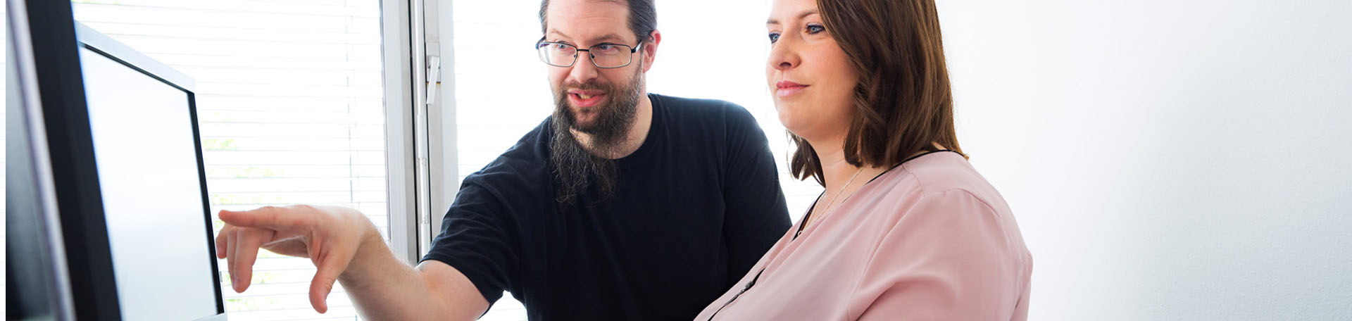Two people sit at a computer. One person points to the screen.